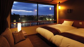 A hotel room with a large window, two beds, a sofa, and a nightstand with a lamp. - Kintarouonsen (Uozu)