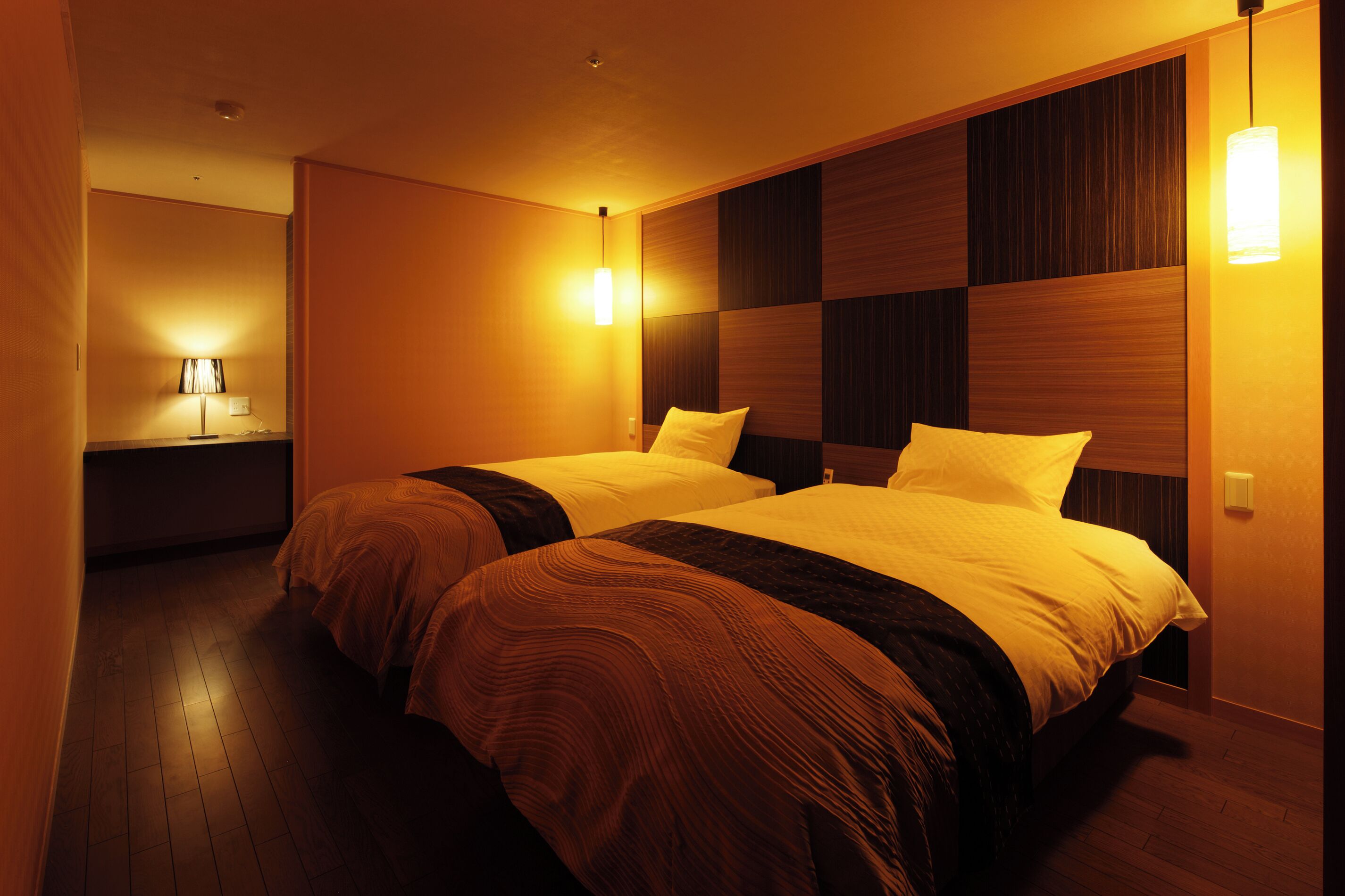Une chambre d’hôtel avec deux lits, des murs recouverts de lambris en bois et une table de chevet avec une lampe.
