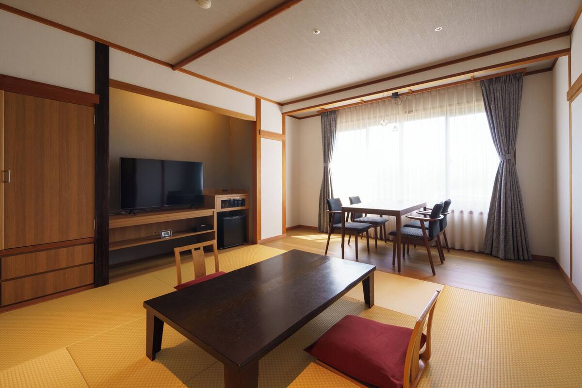 A traditional Japanese-style room with tatami flooring, a low table, chairs, a television, and a sliding door.