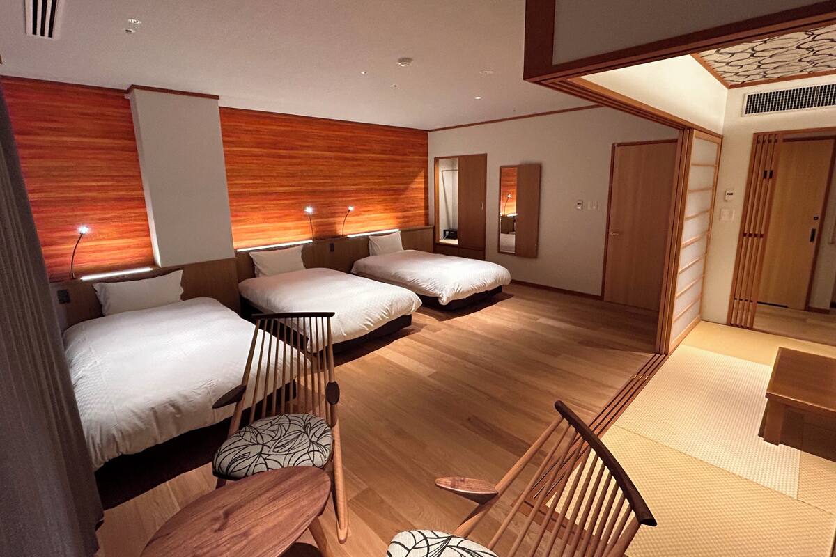A modern hotel room with two beds, a wooden floor, and a small seating area.