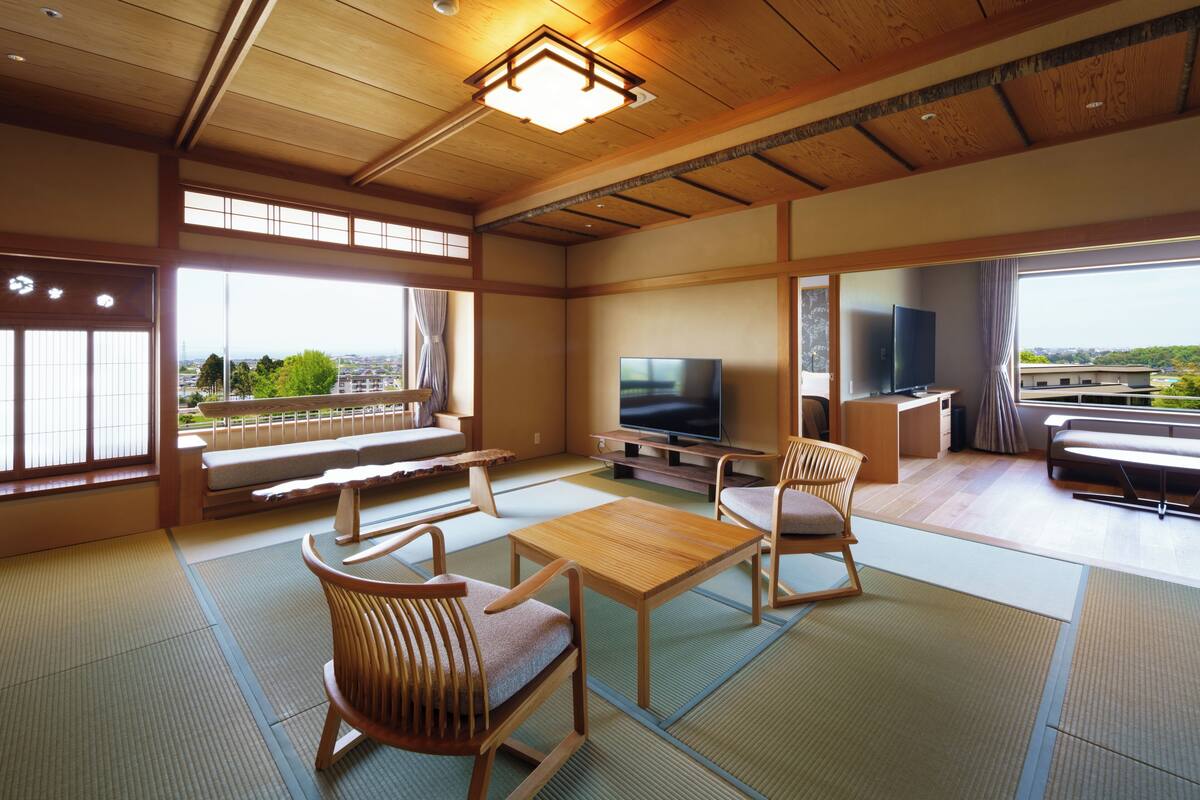 A traditional Japanese room with tatami flooring, a television, and a view of the city.
