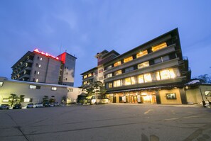 A multi-story hotel with a ground-level entrance and a parking lot. - Kintarouonsen (Uozu)
