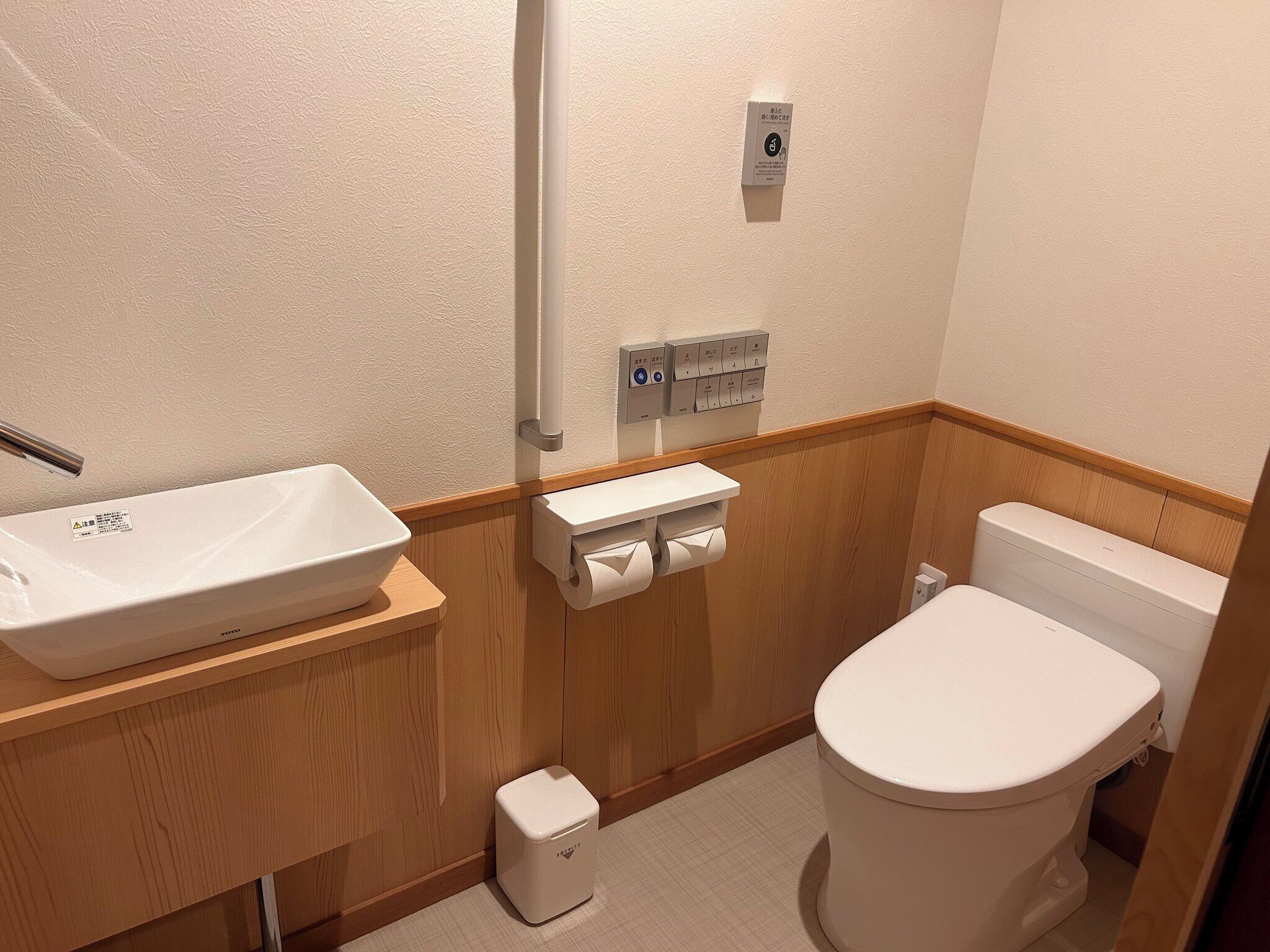 A small bathroom with a white sink, toilet, and a small trash bin.