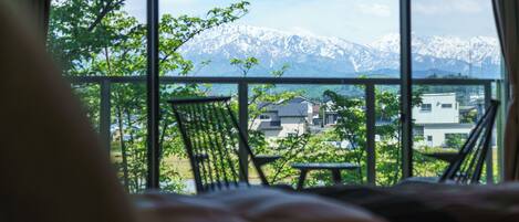 A room with a view of snow-capped mountains and a balcony with chairs.