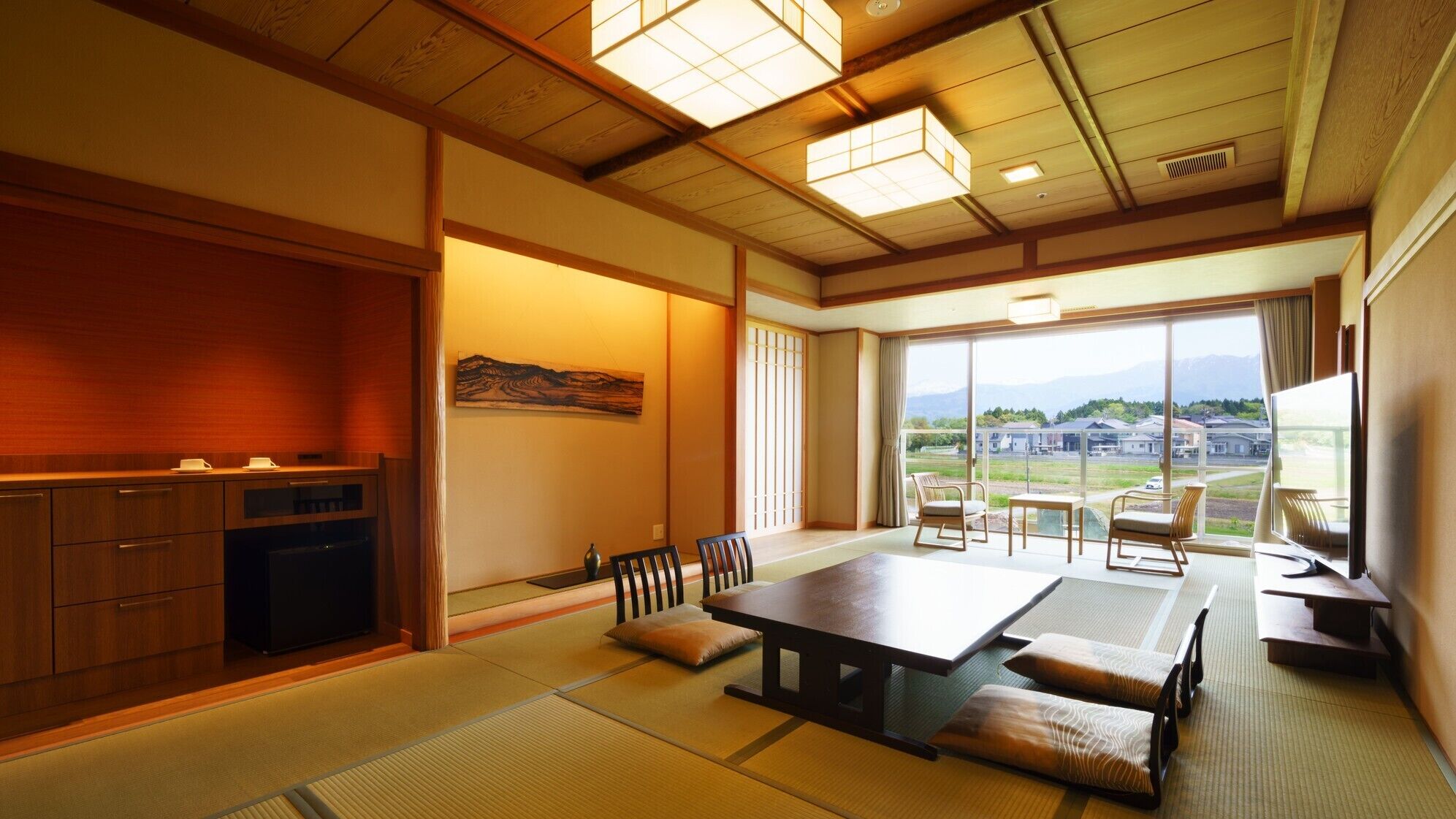 A traditional Japanese room with tatami flooring, a low table, chairs, a television, and a view of a residential area.