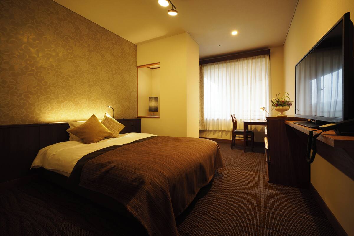 A hotel room with two beds, a desk, a chair, a TV, and a window with curtains.