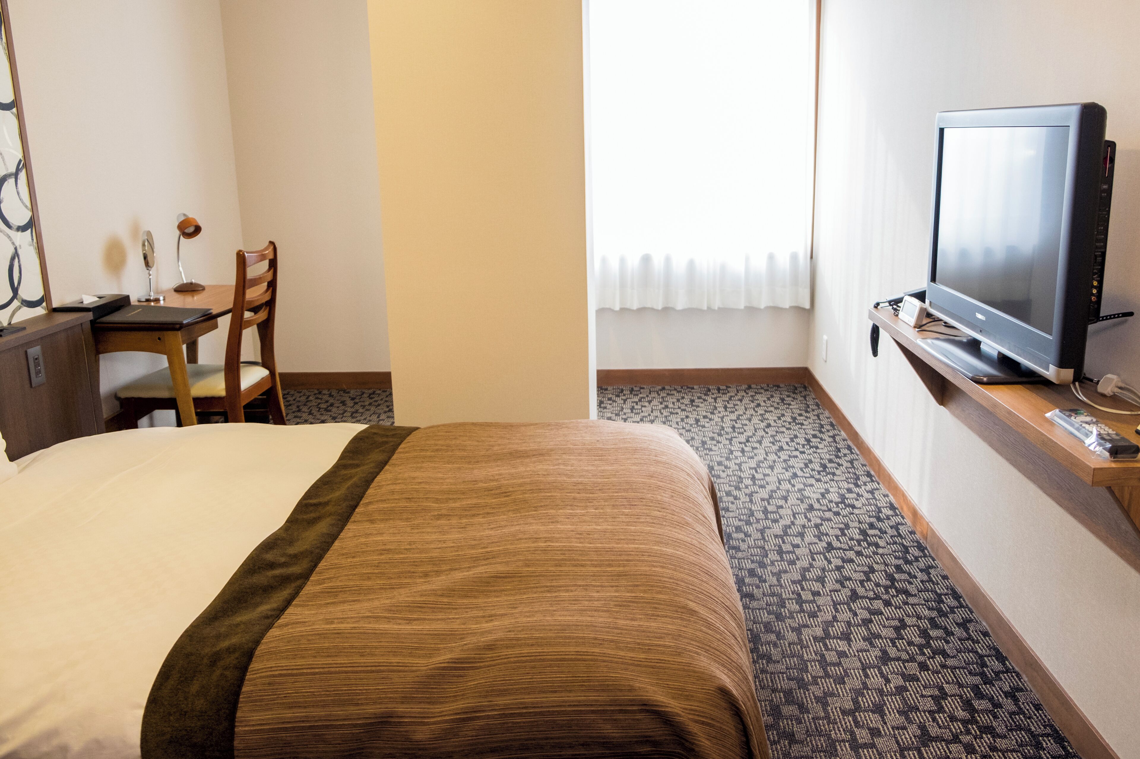 Hotelkamer met een bed, bureau, stoel, televisie en raam met gordijnen.