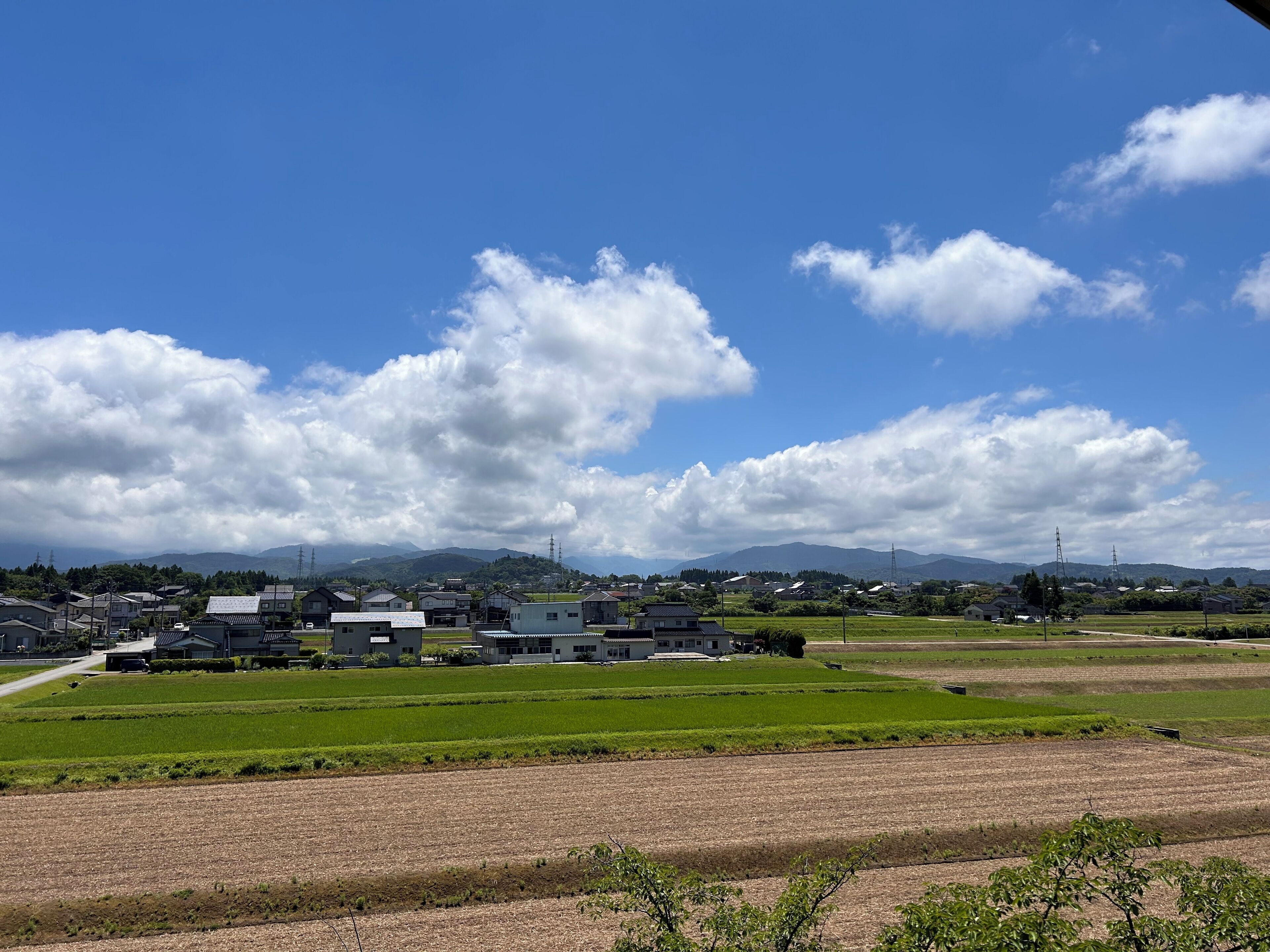 A rural landscape with fields, houses, and mountains in the background.
