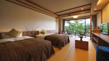 A hotel room with two beds, a sofa, a TV, and a balcony with a view of greenery.