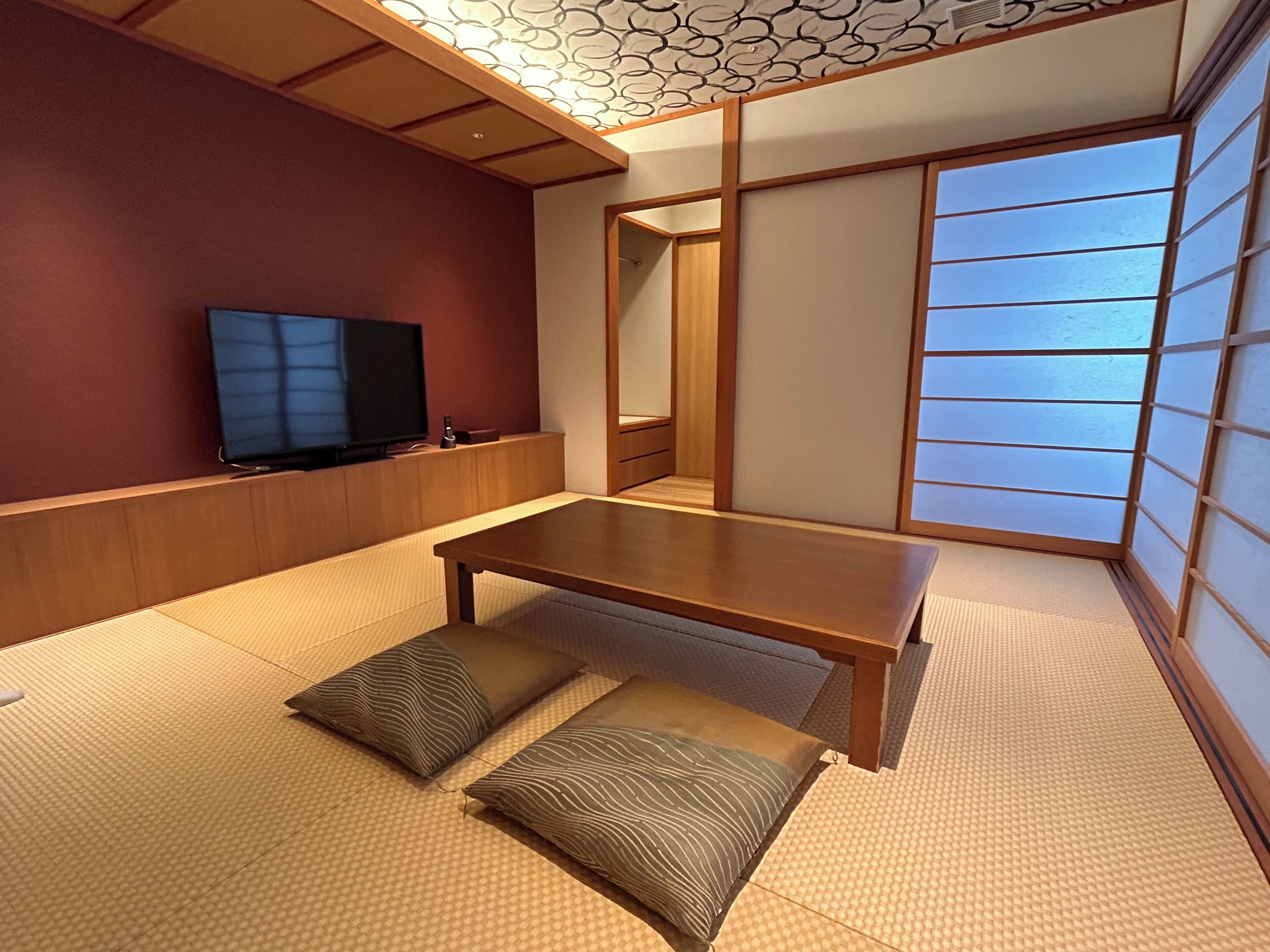 A traditional Japanese room with tatami flooring, a low wooden table, a television, and shoji screens.