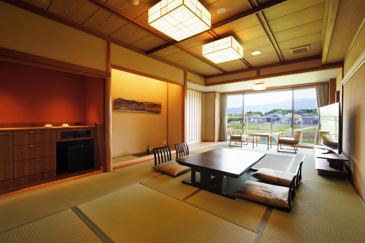 A traditional Japanese room with tatami flooring, a low table, and a view of a mountainous landscape.