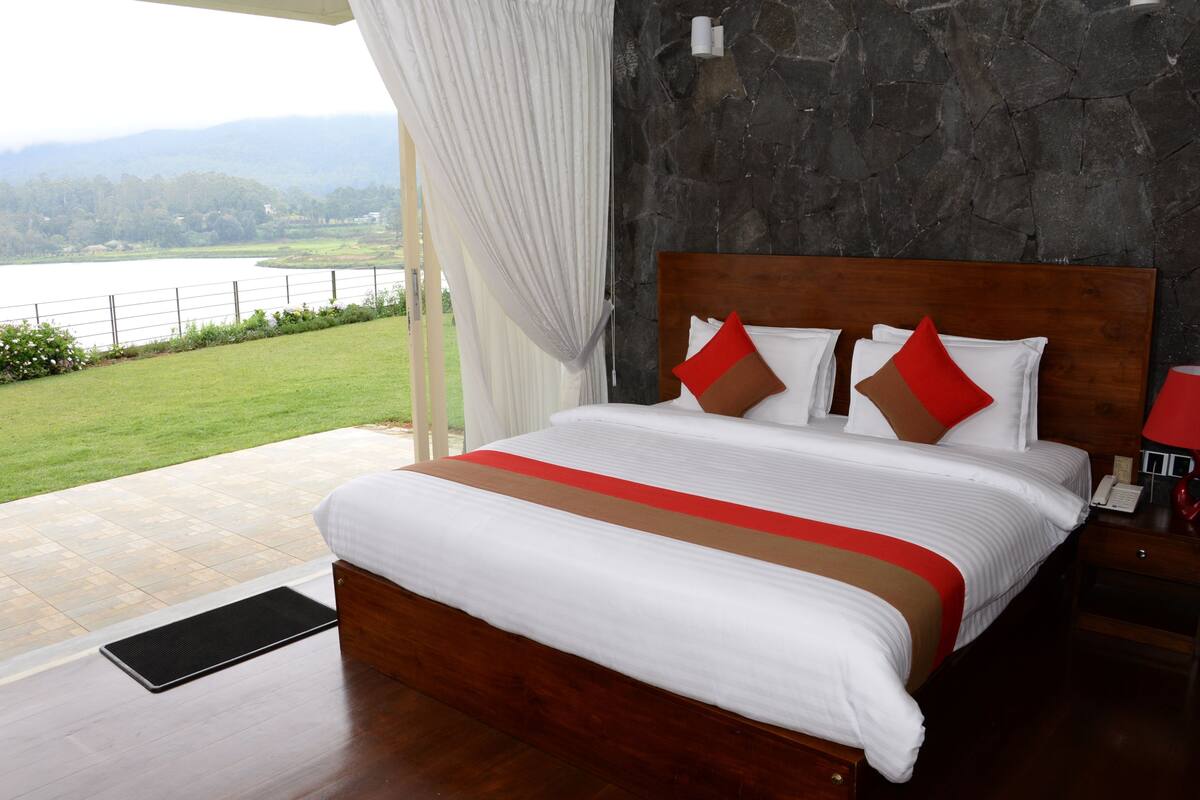 A bedroom with a large bed, a stone wall, and a view of a lake.