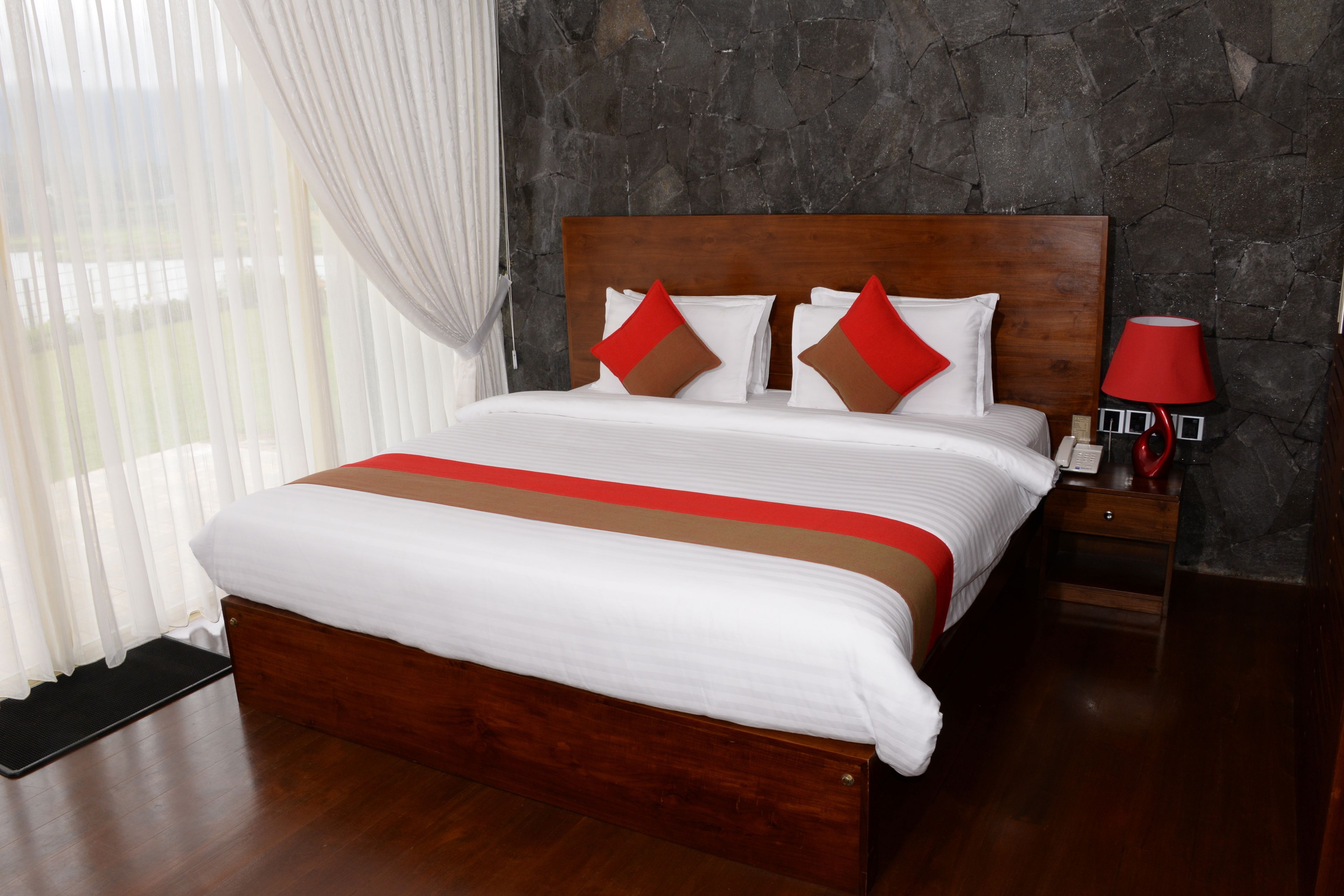 A neatly made bed with a wooden headboard, white bedding, and red accents.