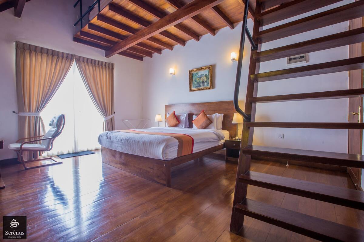 A hotel room with a wooden bed, a chair, a desk, and a staircase.