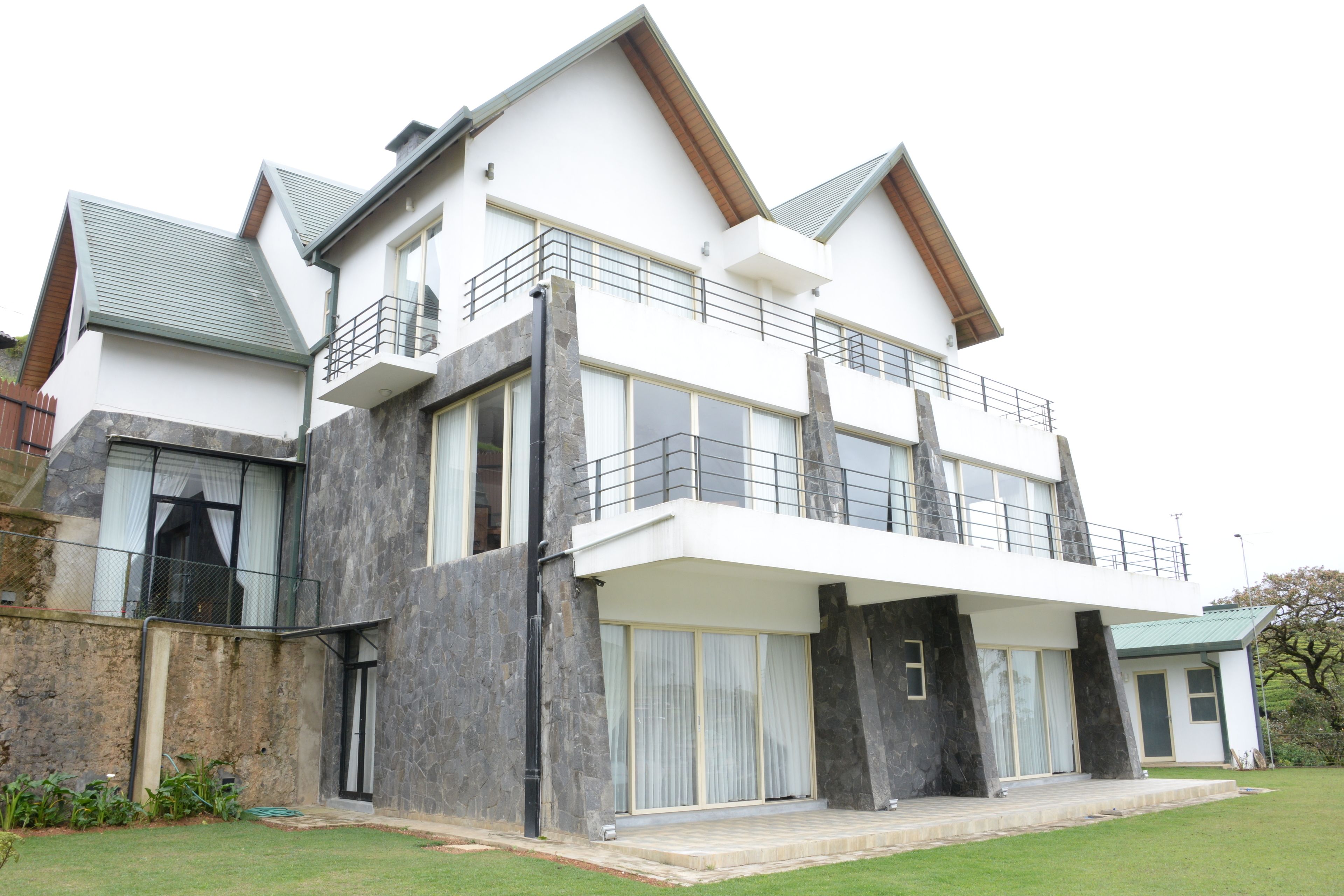 A modern two-story house with a balcony, large windows, and a stone facade.