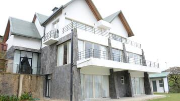 A modern two-story house with a balcony, large windows, and a stone facade.