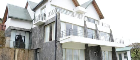 A modern two-story house with a balcony, large windows, and a stone facade.