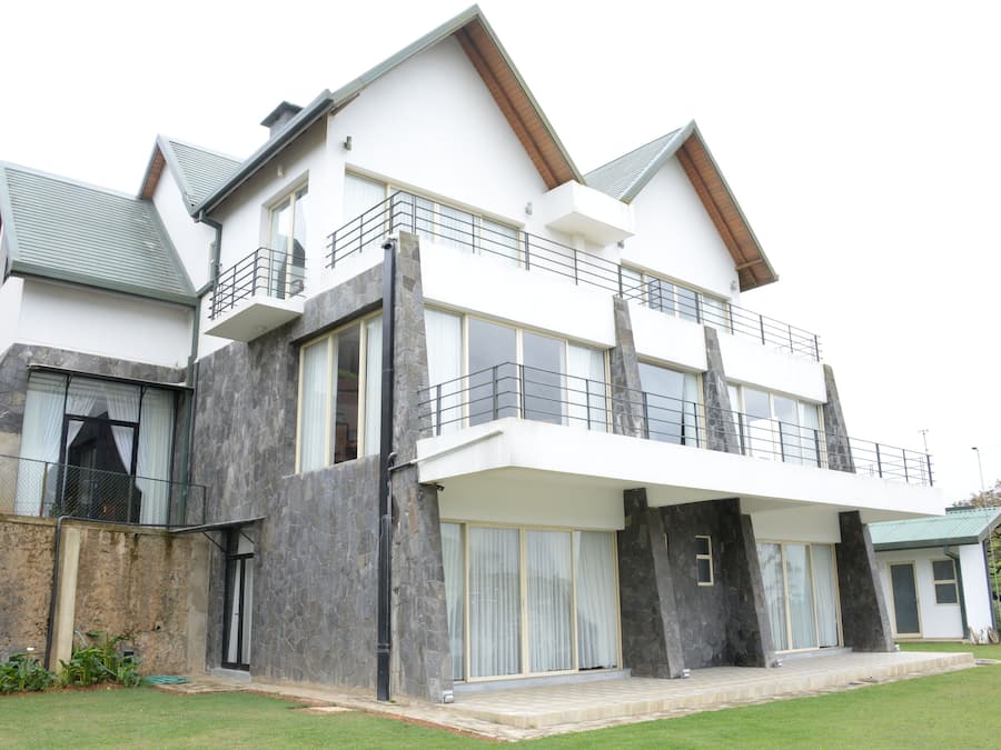 A modern two-story house with a balcony, large windows, and a stone facade.