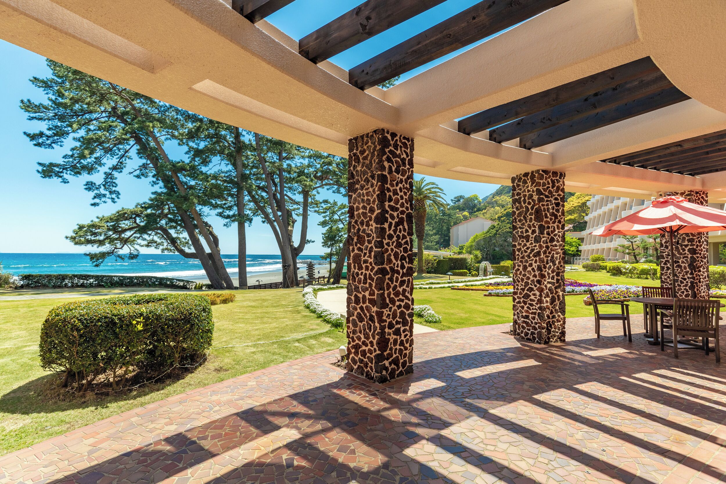 A covered patio area with a view of the ocean, featuring giraffe-patterned columns, a tiled floor, and outdoor furniture.