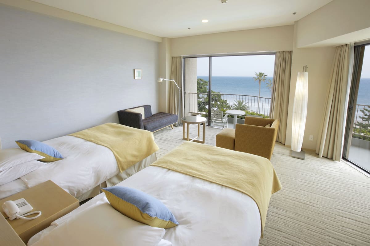Hotelkamer met twee bedden, een slaapbank, een kleintje tafeltje en een balkon met uitzicht op zee.