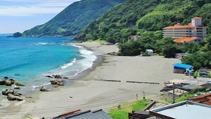 A coastal hotel with a beach view, surrounded by lush greenery and mountains.