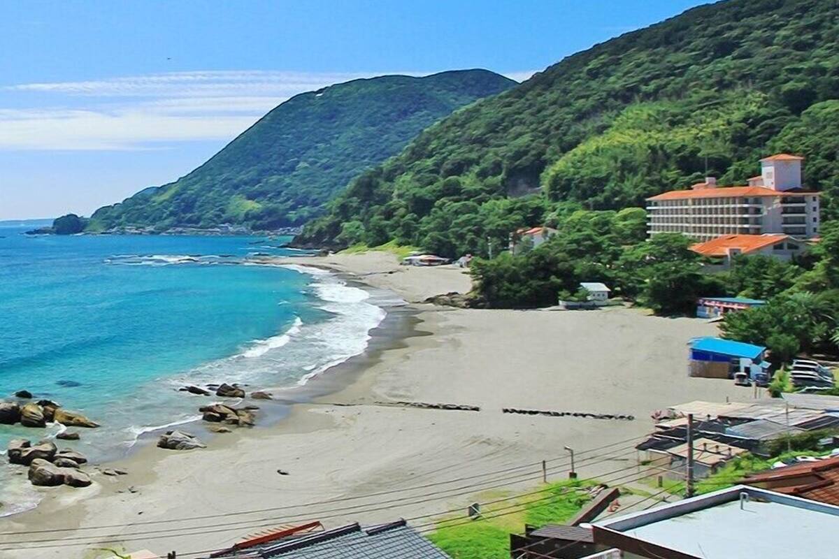 Un hôtel en bord de mer offrant une vue sur la plage, entouré d’une végétation luxuriante et de montagnes.