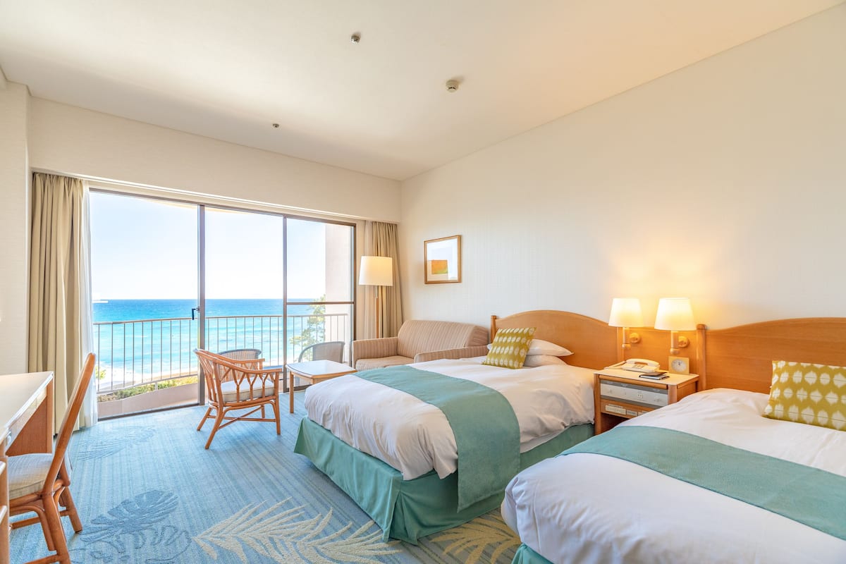 Une chambre d’hôtel avec deux lits, un balcon donnant sur la mer, un bureau et une chaise.