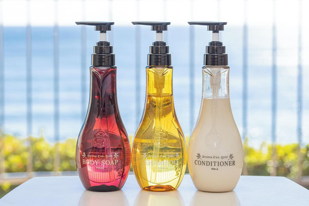 Trois bouteilles de savon pour le corps, de shampoing et d’après-shampoing sont posées sur une table, avec en arrière-plan une vue sur des bâtiments.