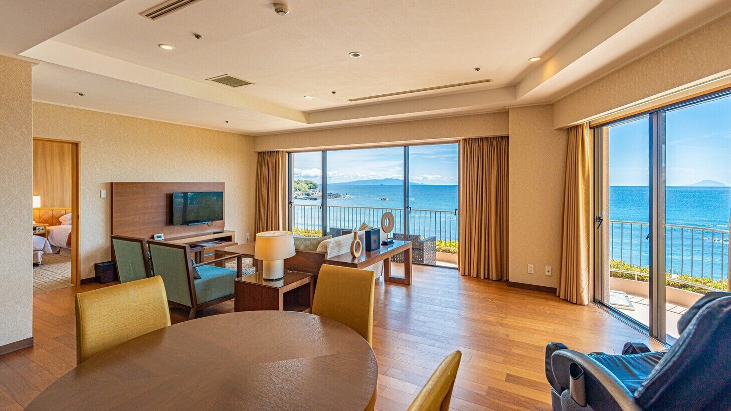 Habitación de hotel con balcón grande, televisión, zona de comedor y vista al mar.