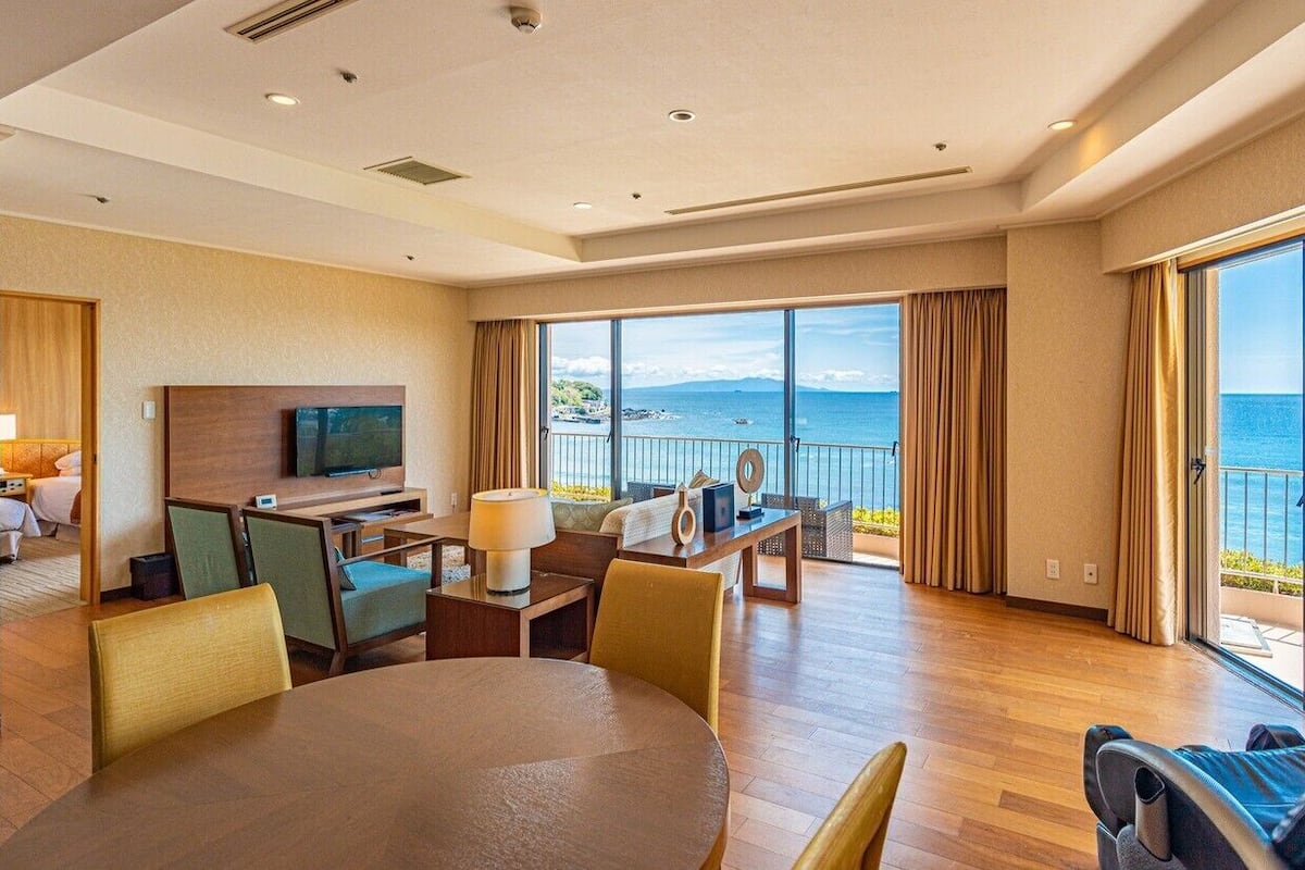 Une chambre d’hôtel dotée d’un grand balcon, d’une télévision, d’un coin repas et offrant une vue sur la mer.