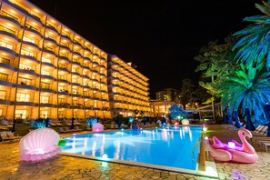 Een hotel met een zwembadgedeelte, versierd met flamingo drijvers en lichtjes in de vorm van schelpen.