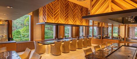 A modern kitchen with a long island, bar seating, and large windows offering a view of the outdoors.