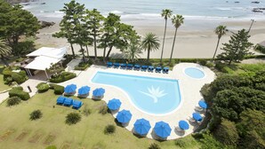 A resort with a swimming pool, beach view, and lounge area with umbrellas.