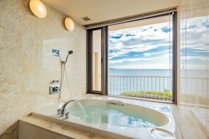 Une salle de bain dotée d’une grande baignoire, d’une douche et offrant une vue sur la mer grâce à une porte-fenêtre coulissante.