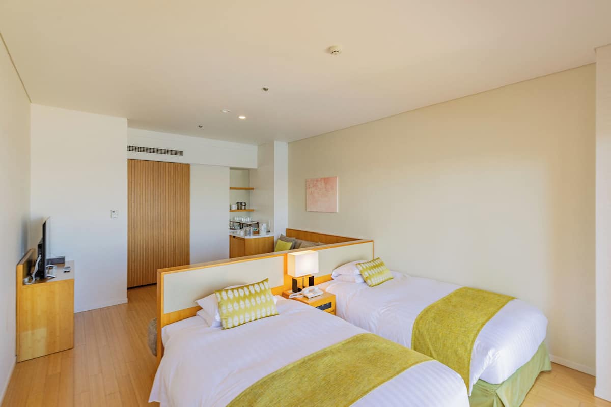 Une chambre d’hôtel avec deux lits, une table de chevet en bois, un bureau avec un ordinateur et un miroir.