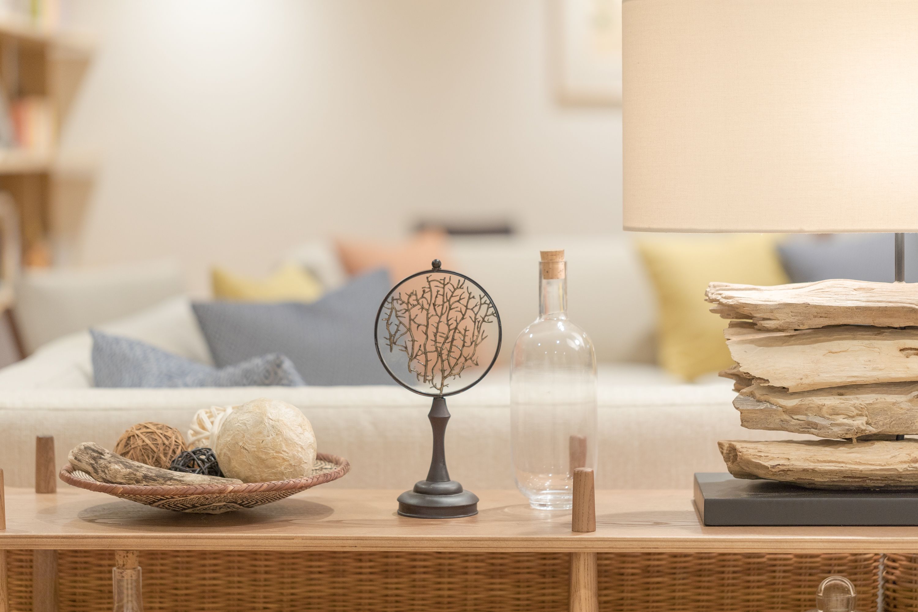 A wicker side table with a decorative tree, a clear bottle, and a stack of books.