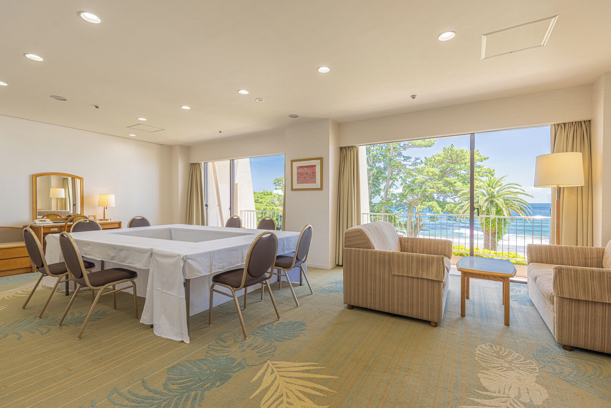 Habitación de hotel con mesa de comedor, sillas, sofá y balcón con vista al océano.