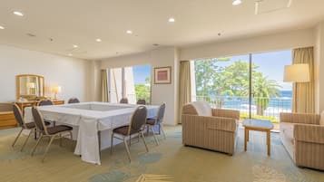 A hotel room with a dining table, chairs, a sofa, and a balcony with a view of the ocean.