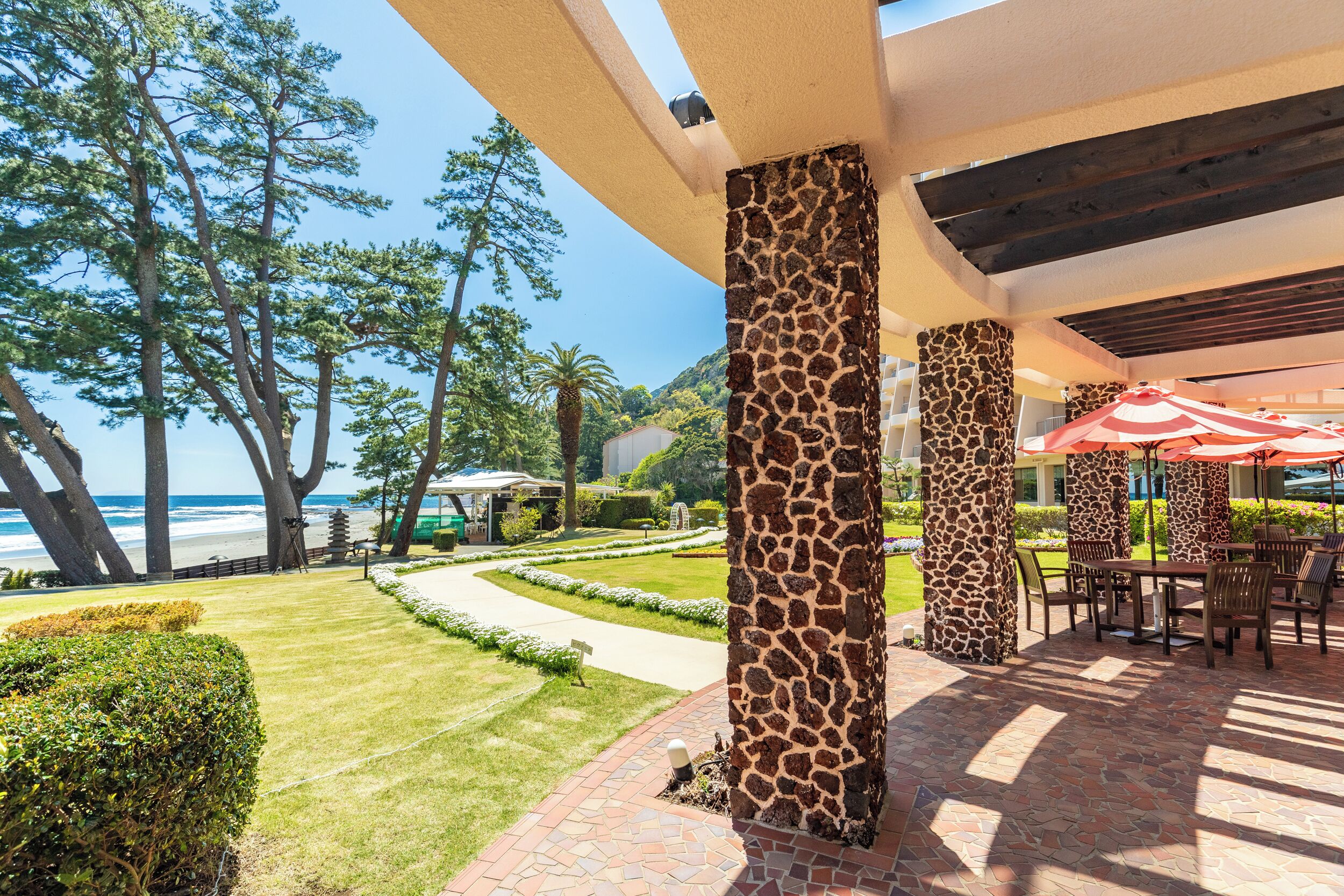 Un patio al aire libre con columnas con motivos de jirafa, un camino empedrado y vista a la playa.