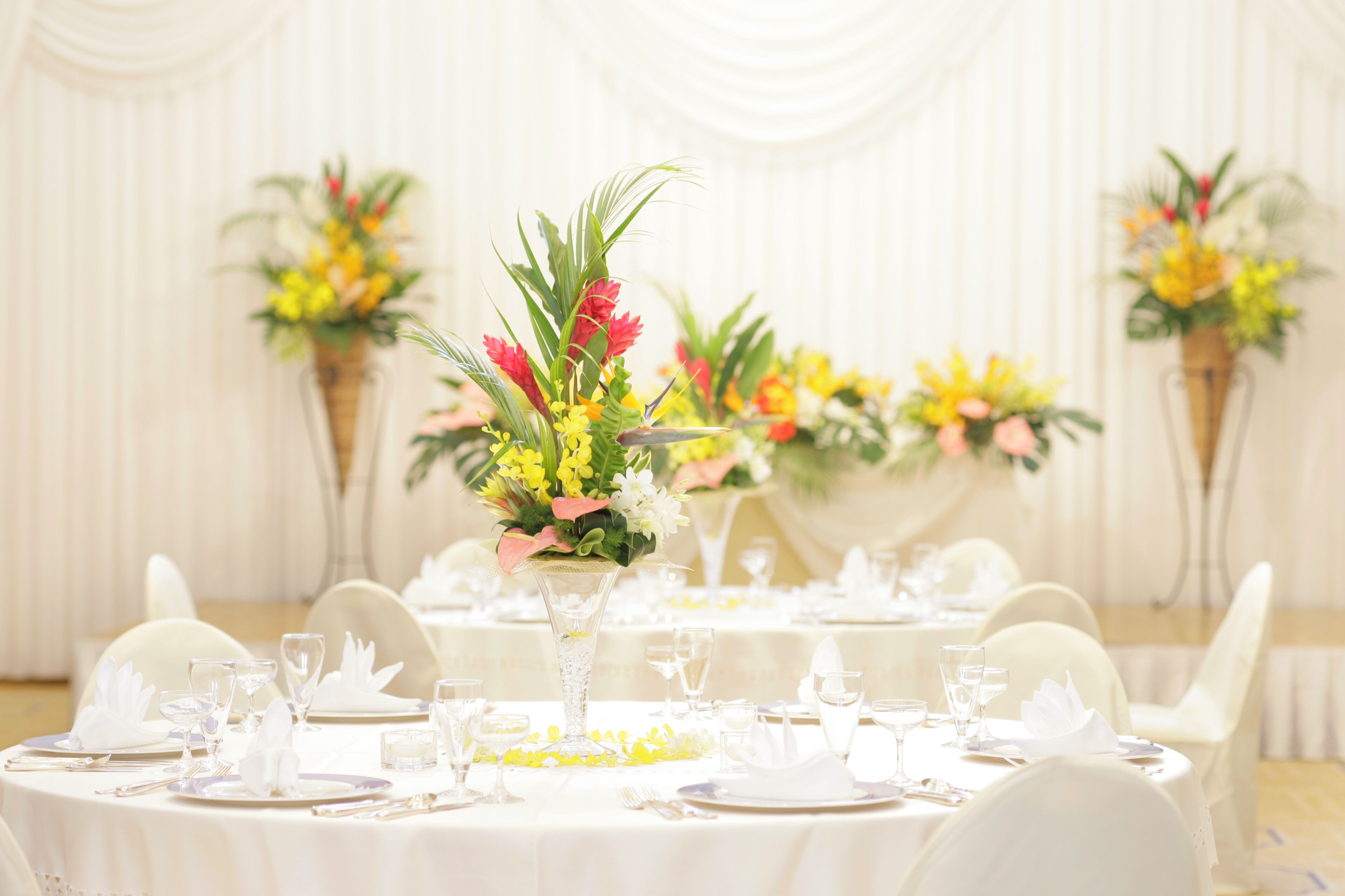 A banquet hall with round tables set for a formal event, featuring white tablecloths, glassware, and floral centerpieces.