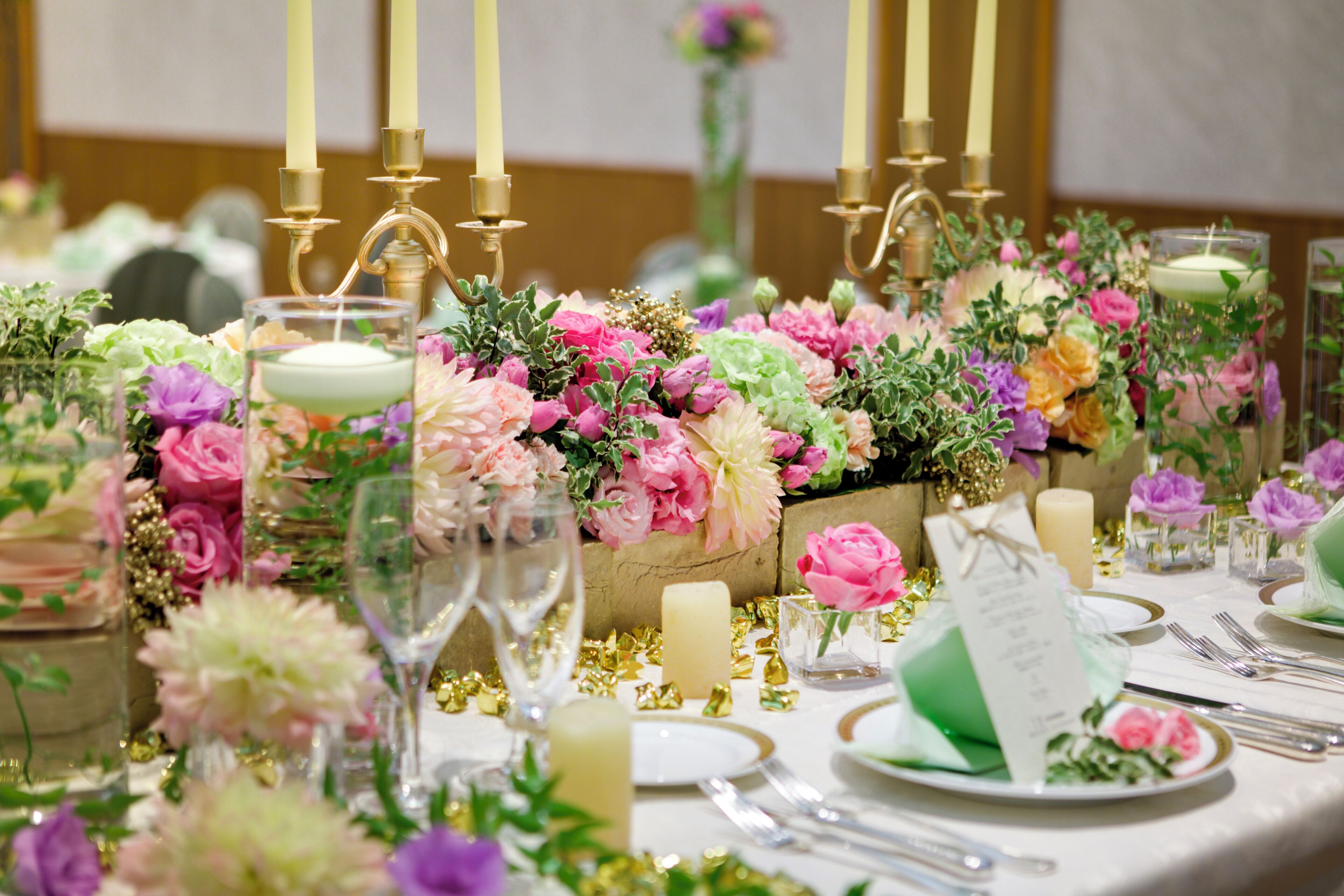 Una mesa dispuesta para un evento formal, con centros de flores, velas y una tarjeta de menú.