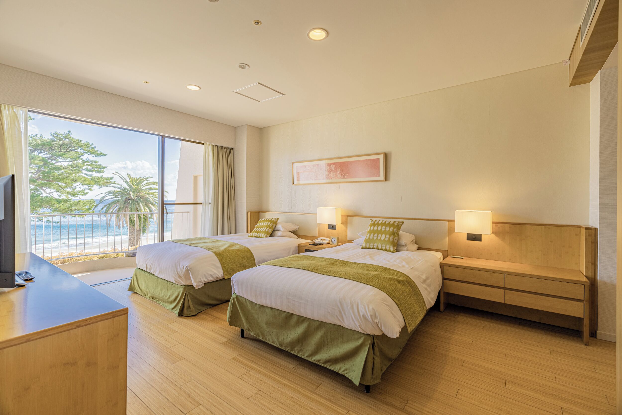 A hotel room with two beds, a desk, and a view of the beach.