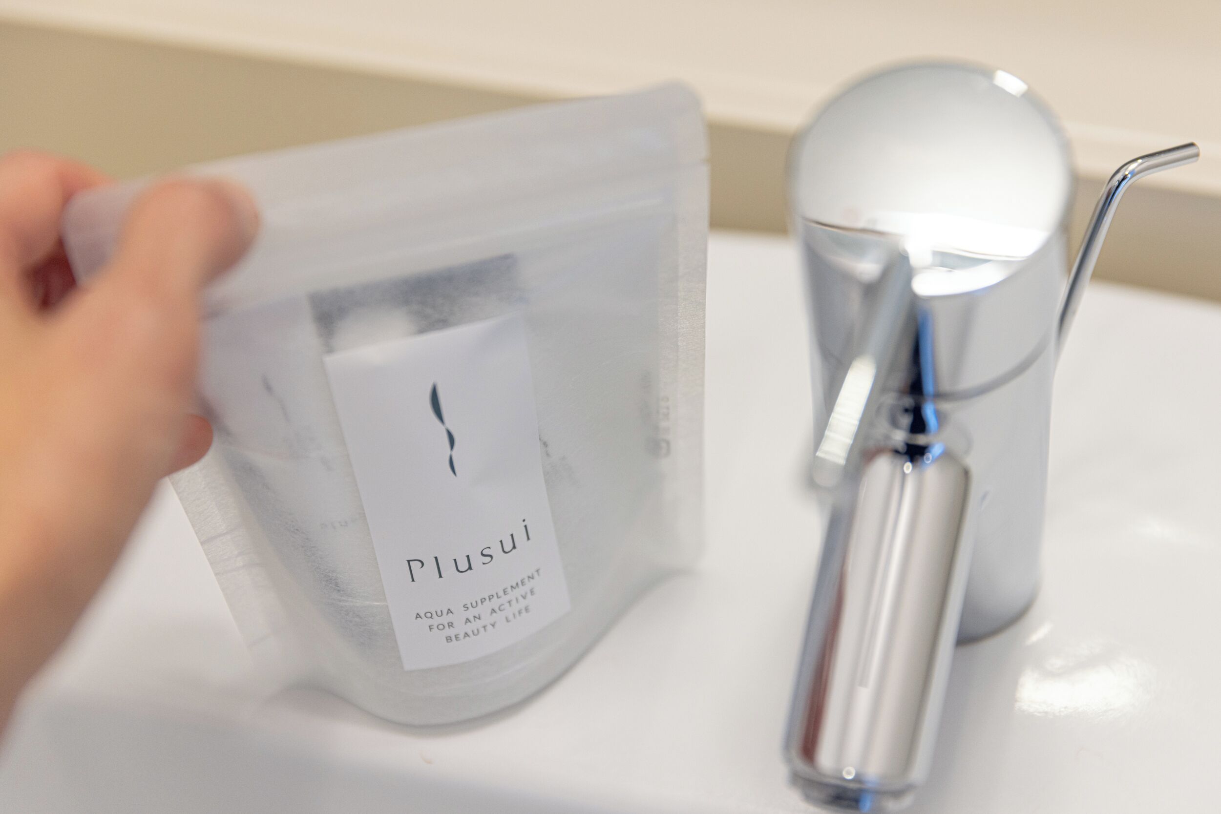 Eine Hand hält eine transparente Plastiktüte mit dem Aufdruck 'Plusui Aqua Supplement für ein aktives Schönheitsleben'.