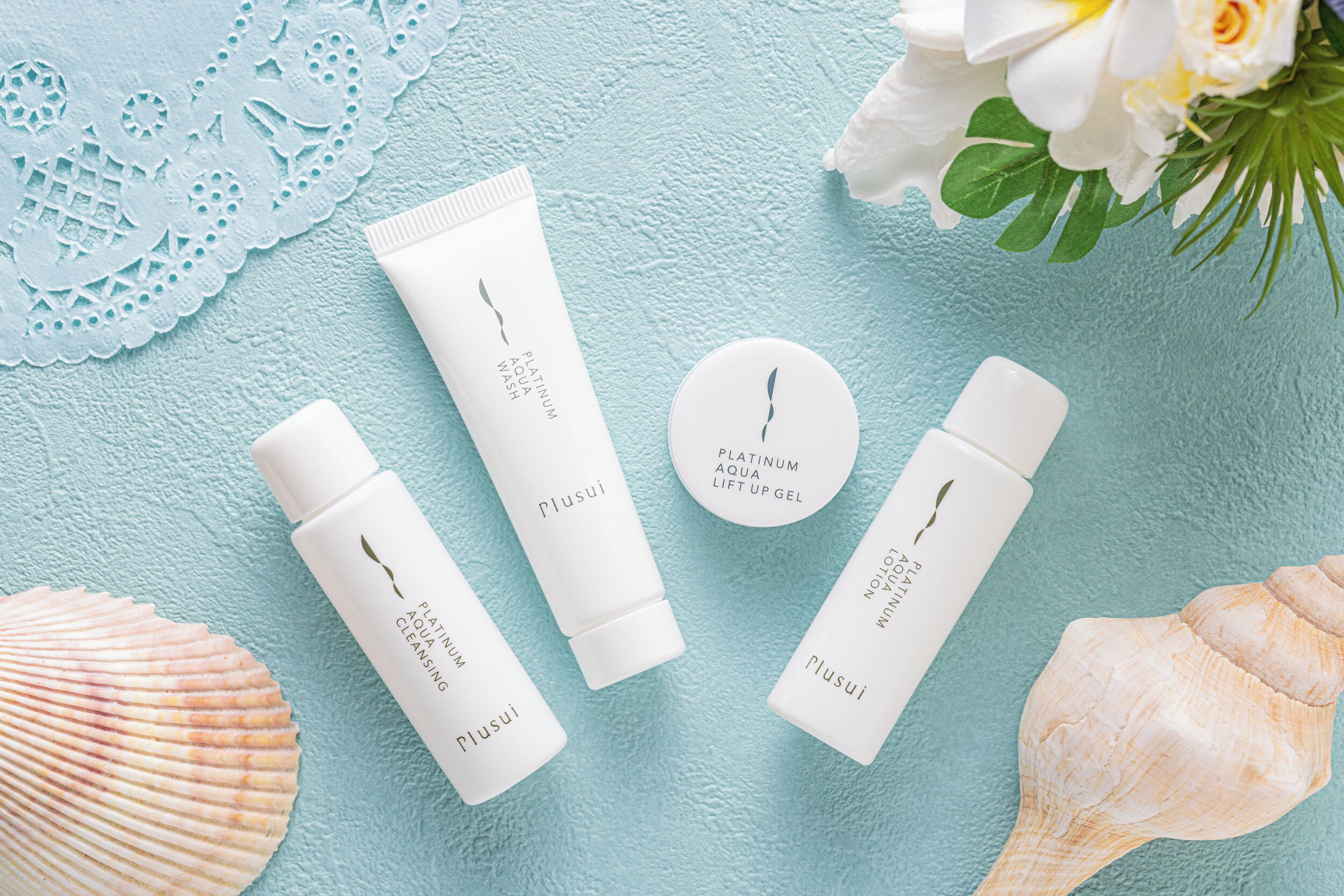 A set of skincare products on a textured blue surface with lace and seashells.