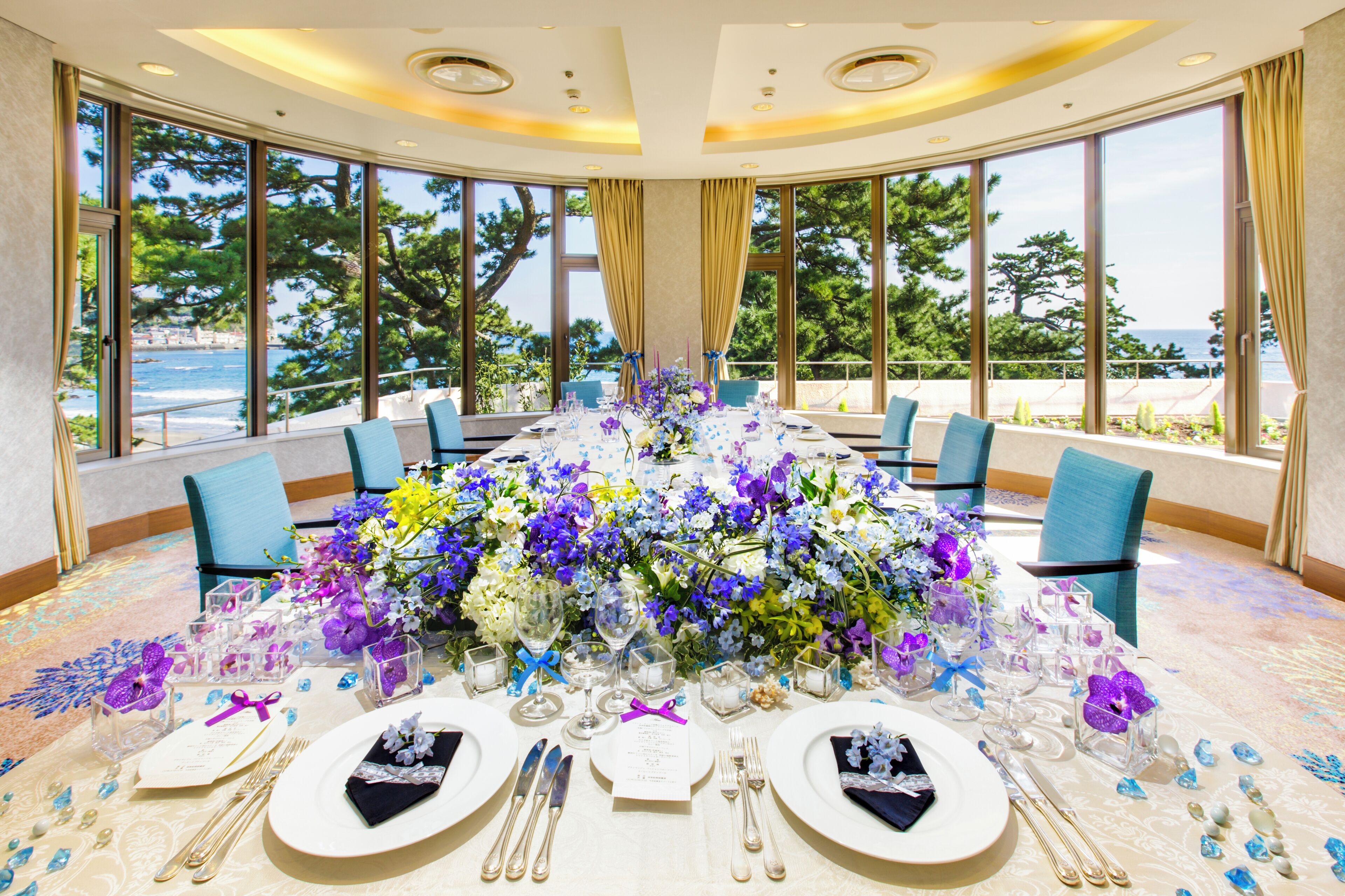 Una mesa redonda dispuesta para un evento formal, con un centro de mesa floral, cristalería transparente y cubertería impecable.