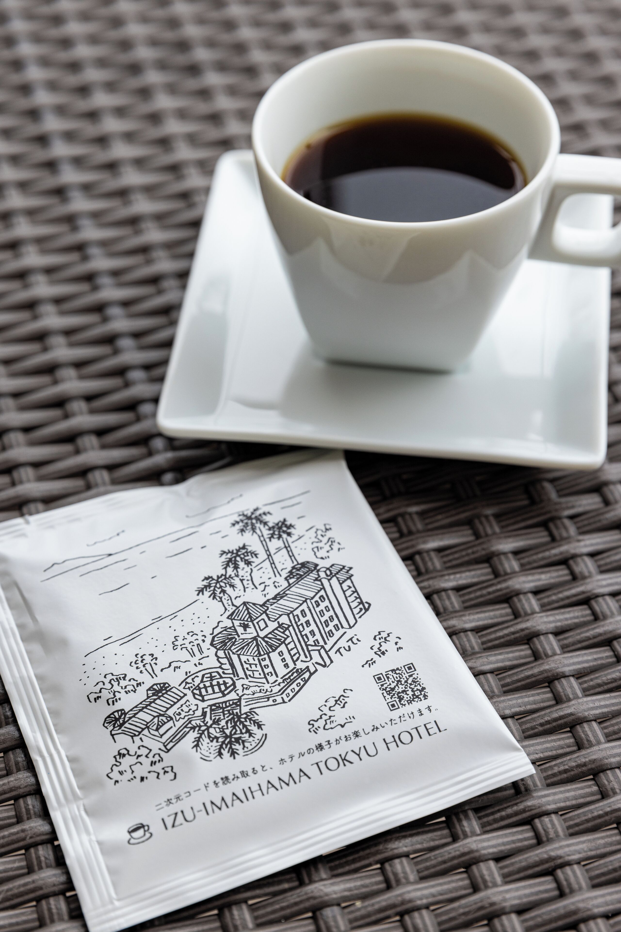 A white cup of coffee on a white saucer with a printed menu on a woven tablecloth.