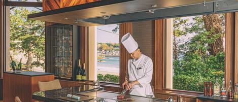 Un chef preparando comida en una barra con vista a la playa y a los árboles.