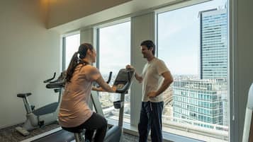 A gym with a treadmill, a stationary bike, and a large window offering a city view.