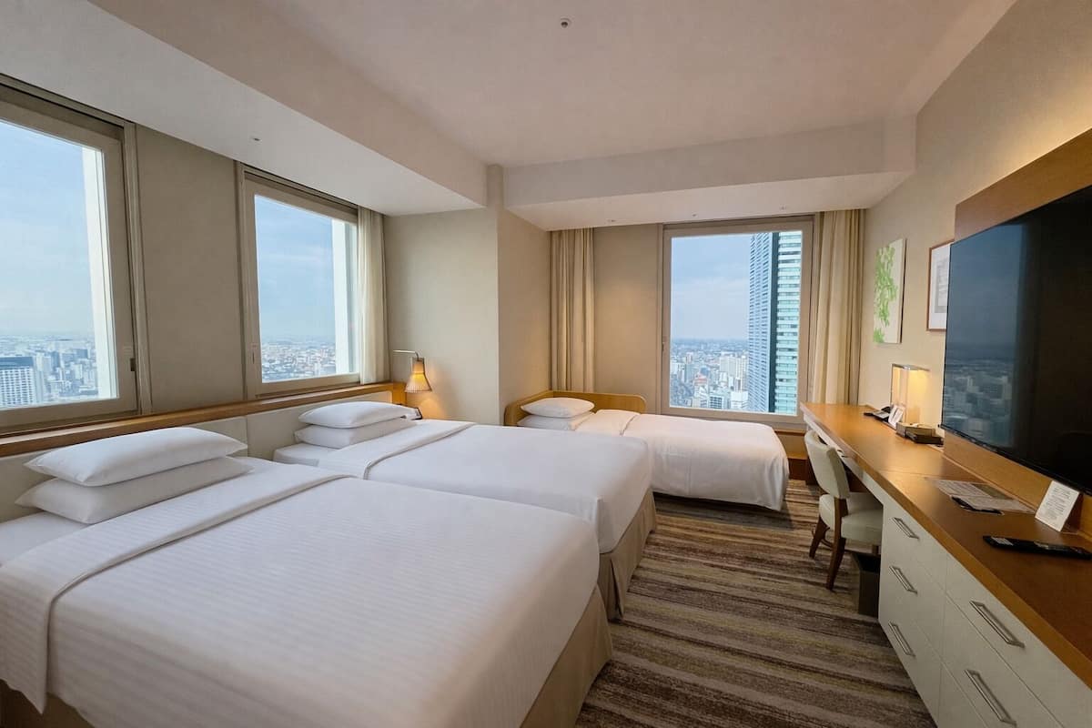 Hotelkamer met twee bedden, een bureau, een televisie en grote ramen met uitzicht op de stad.