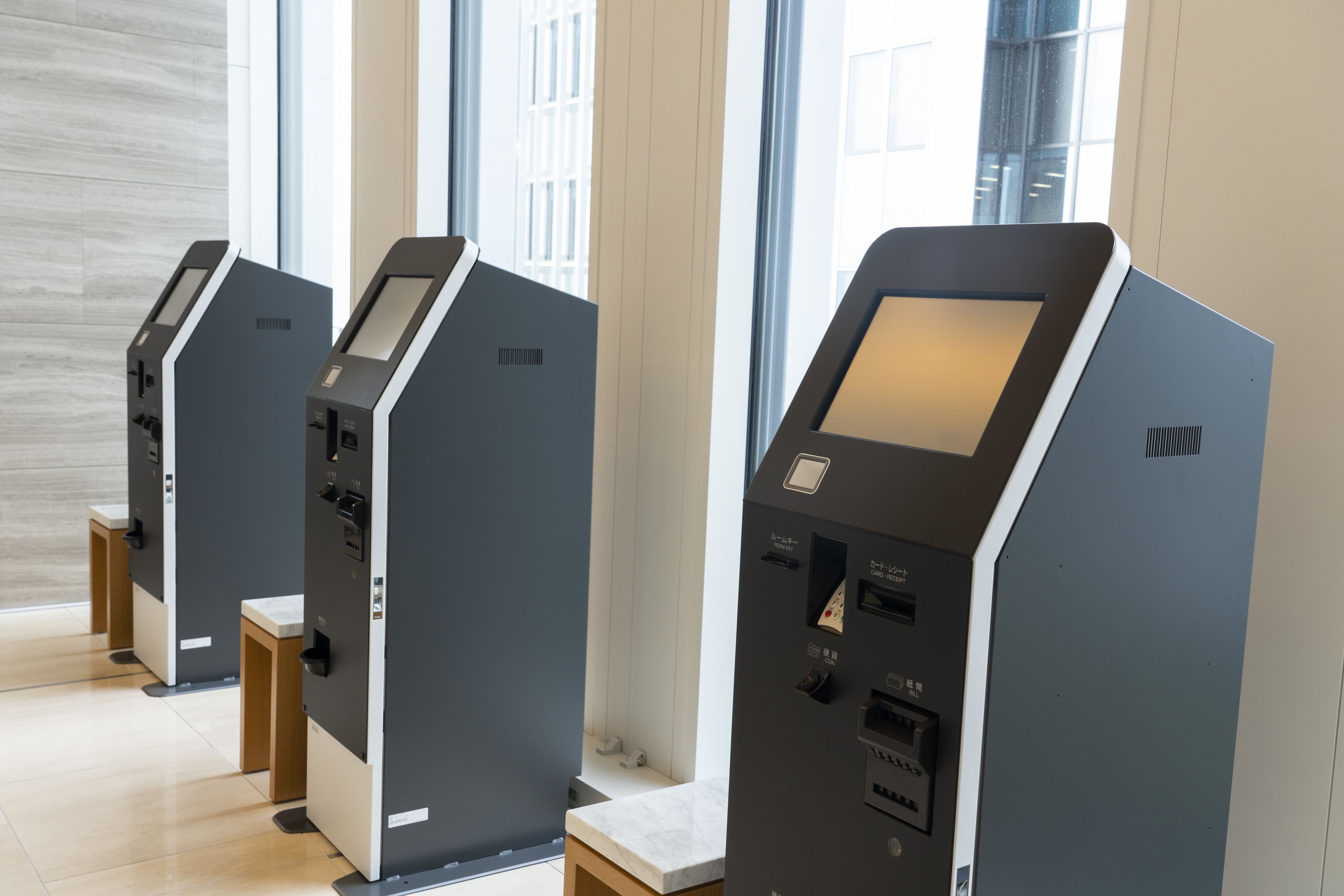 A row of self-service kiosks in a modern indoor setting with large windows.